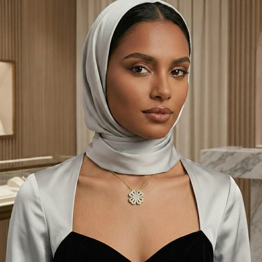Woman wearing a light gray hijab and a necklace with a floral pendant in an indoor setting.
