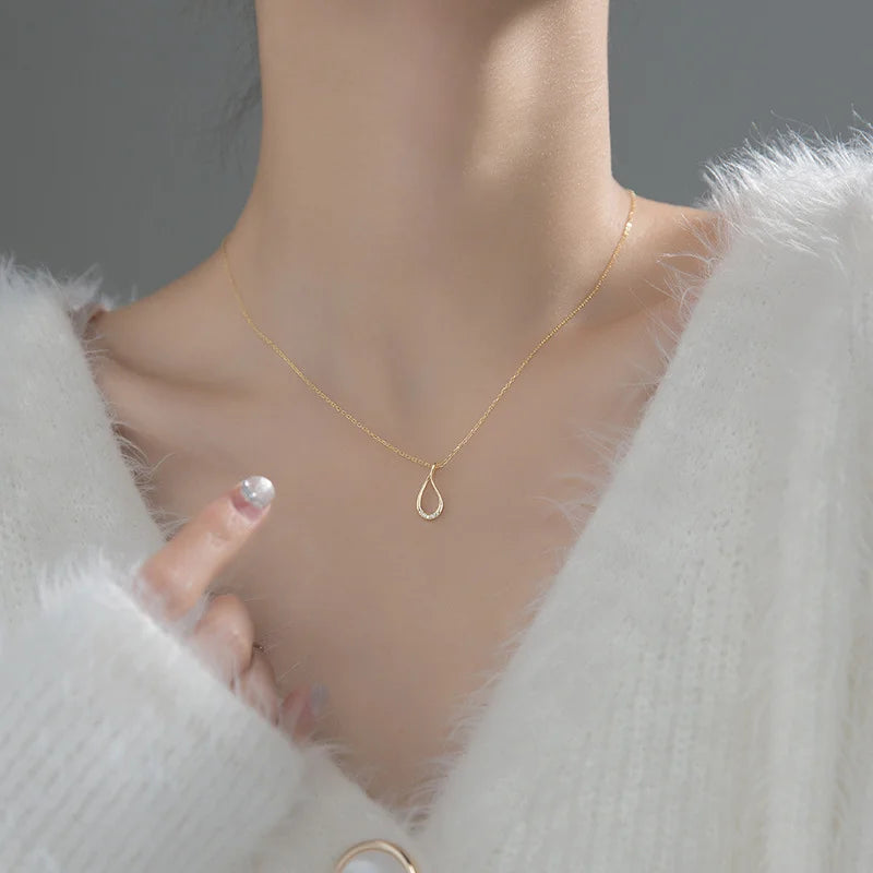 Gold necklace with a teardrop pendant worn by a person in a white coat.