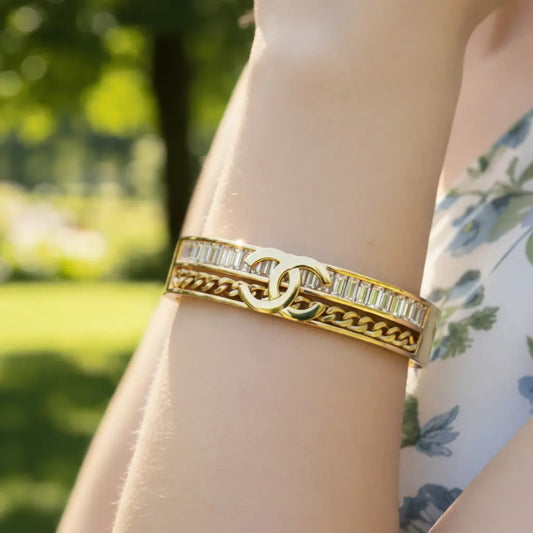 Gold bracelet with gemstones on a wrist against a blurred green outdoor background
