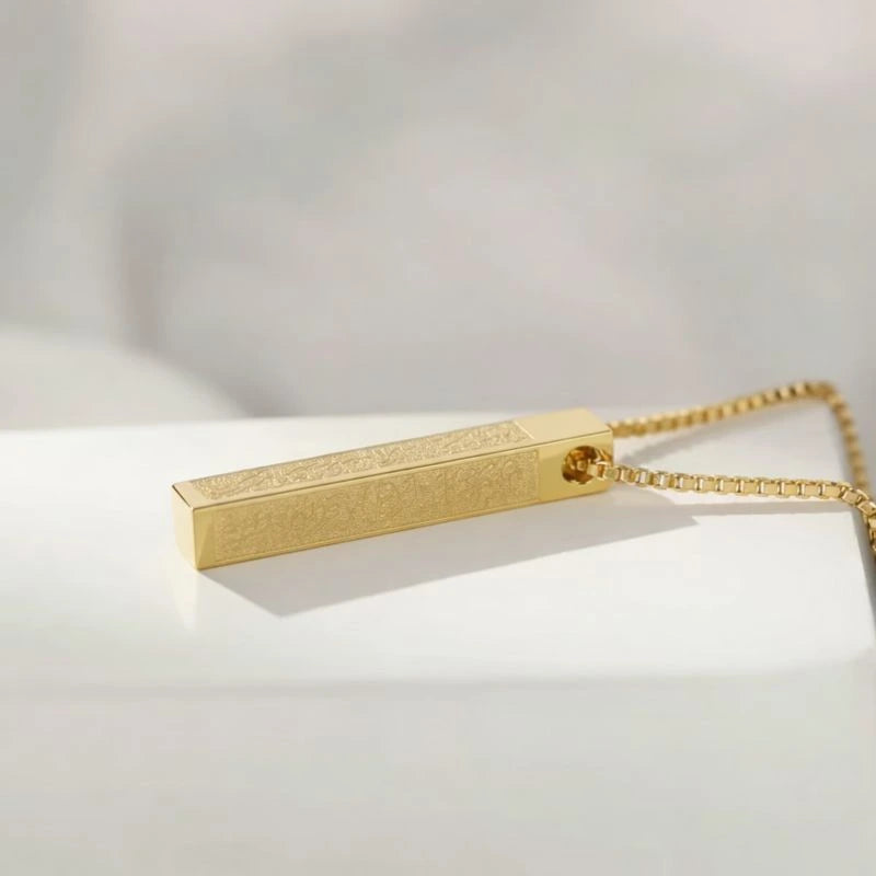 Gold rectangular pendant on a chain against a light background