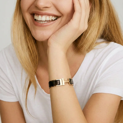 Woman wearing a gold and black bracelet on a plain background