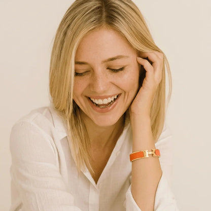 Woman with blonde hair smiling and wearing a white shirt with an orange bracelet.