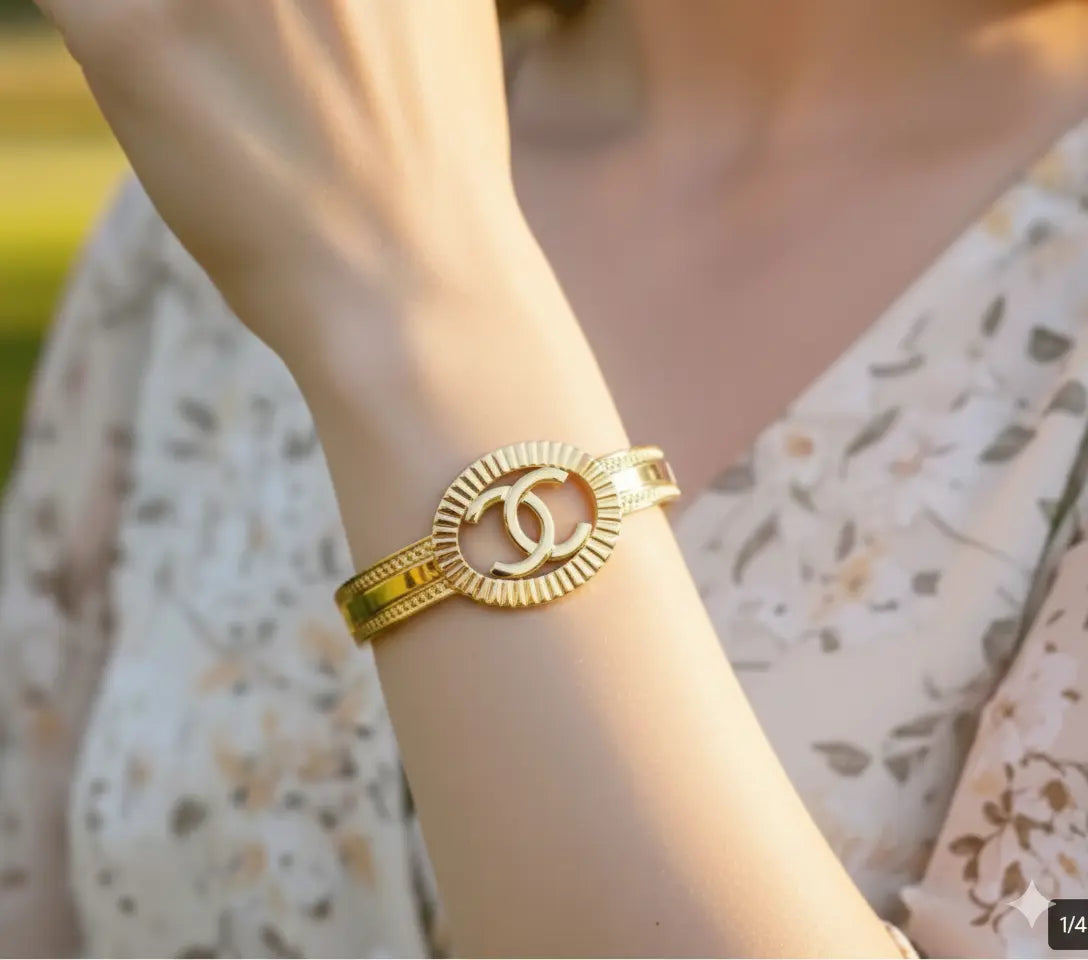 Gold bracelet with a brand logo on a wrist, blurred background