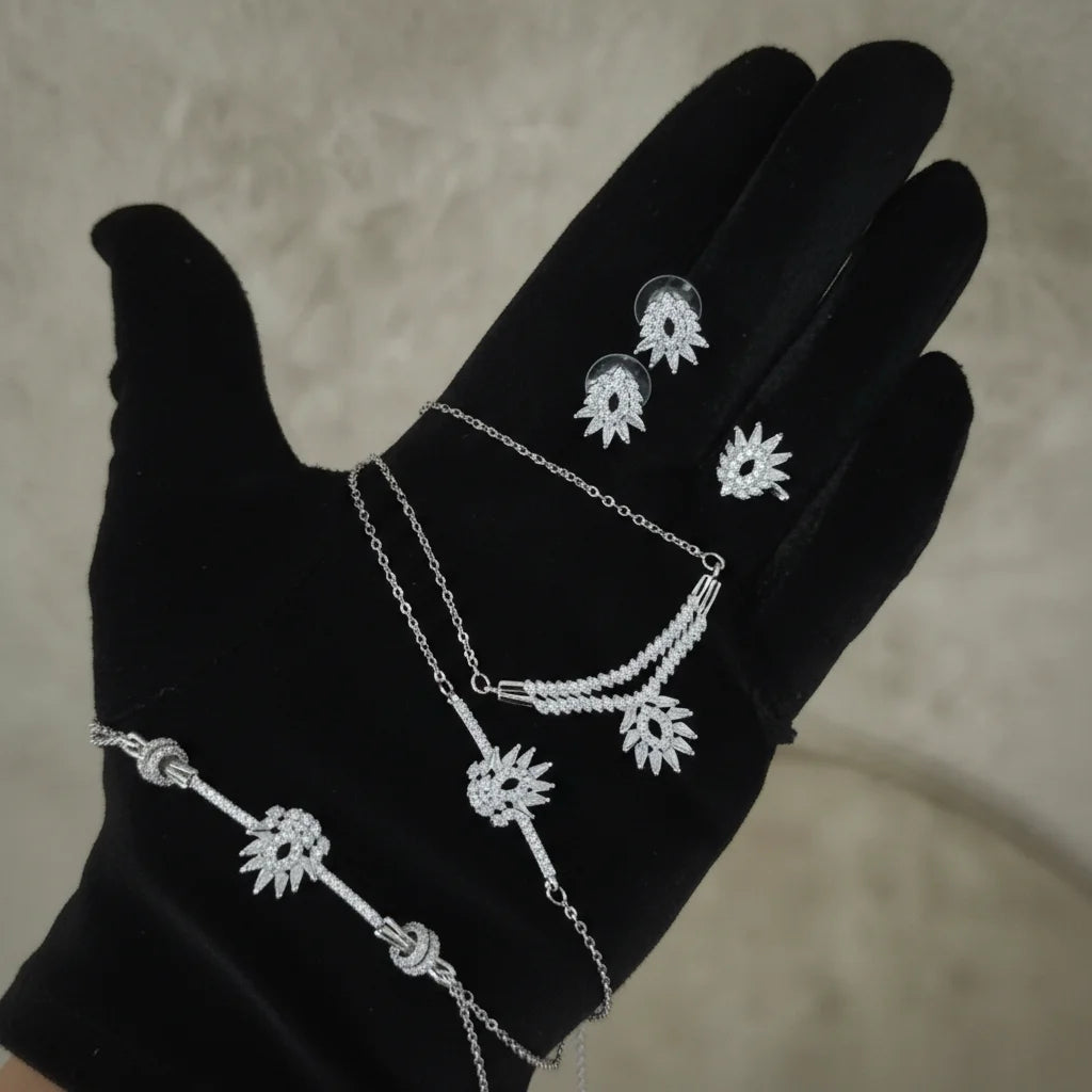 Silver jewelry set on a black glove against a neutral background