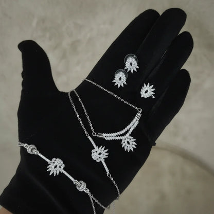 Silver jewelry set on a black glove against a neutral background