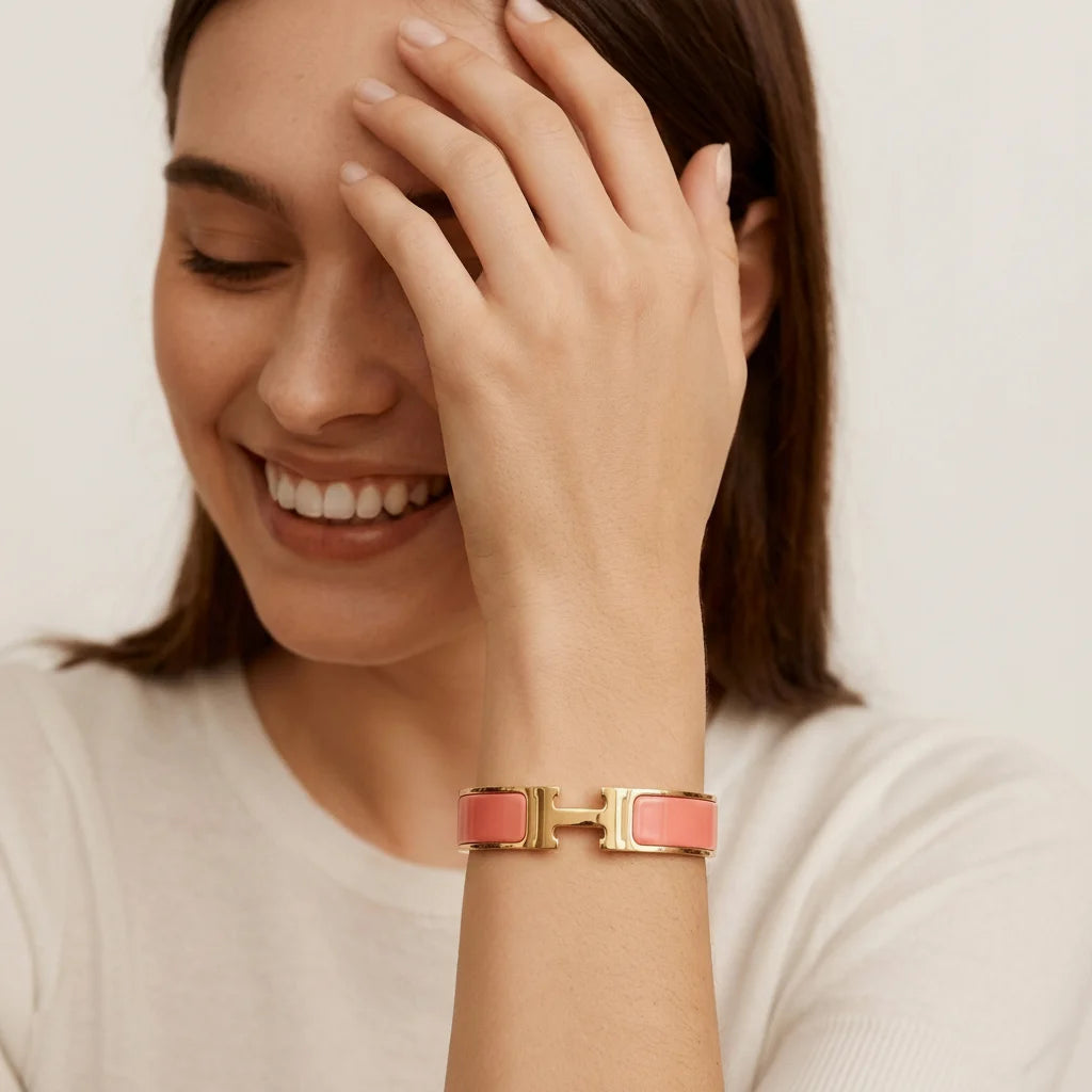 Woman wearing a gold bracelet with a pink accent on a plain background