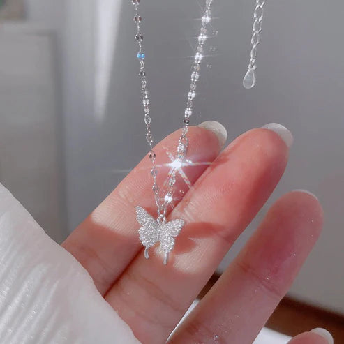 Silver butterfly pendant necklace on a hand with a blurred background