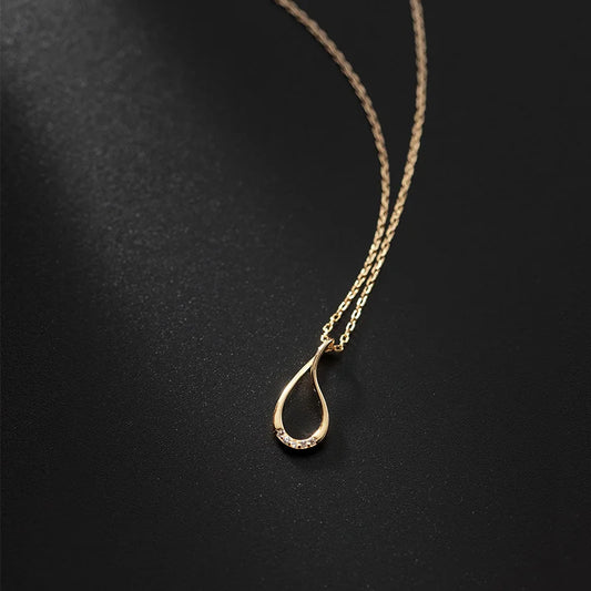 Gold necklace with a teardrop pendant on a black background