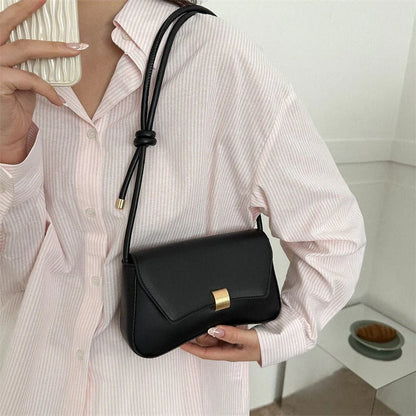 Person holding a black handbag with a gold clasp in a minimal indoor setting