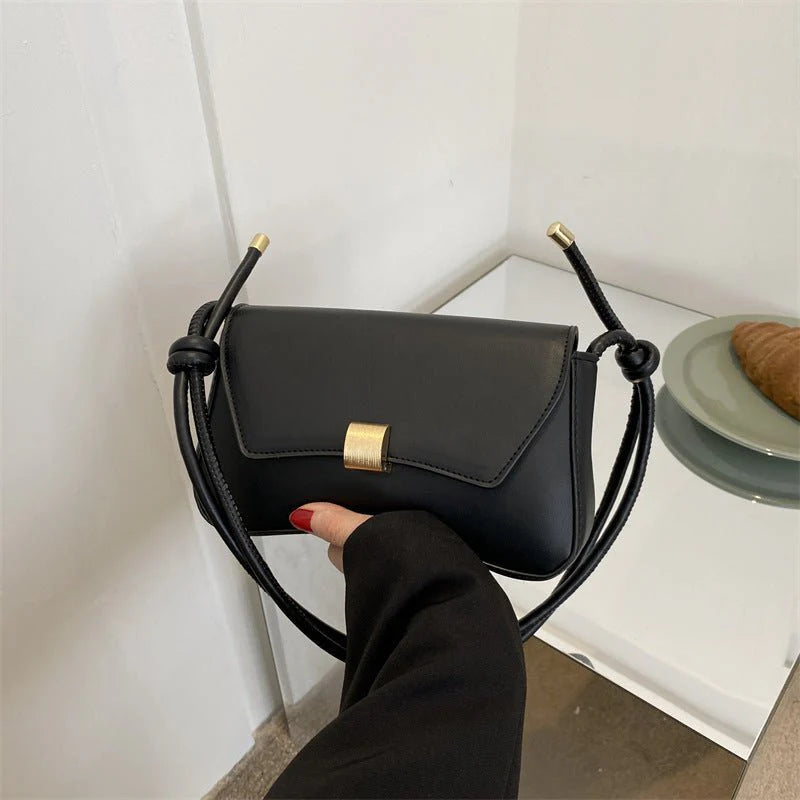 Black handbag with gold accents held by a person against a white wall.
