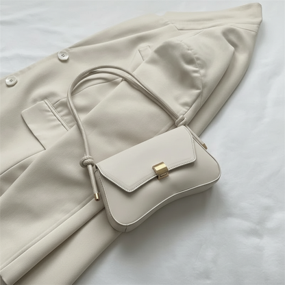 White handbag with gold accent held by a hand on a light-colored coat