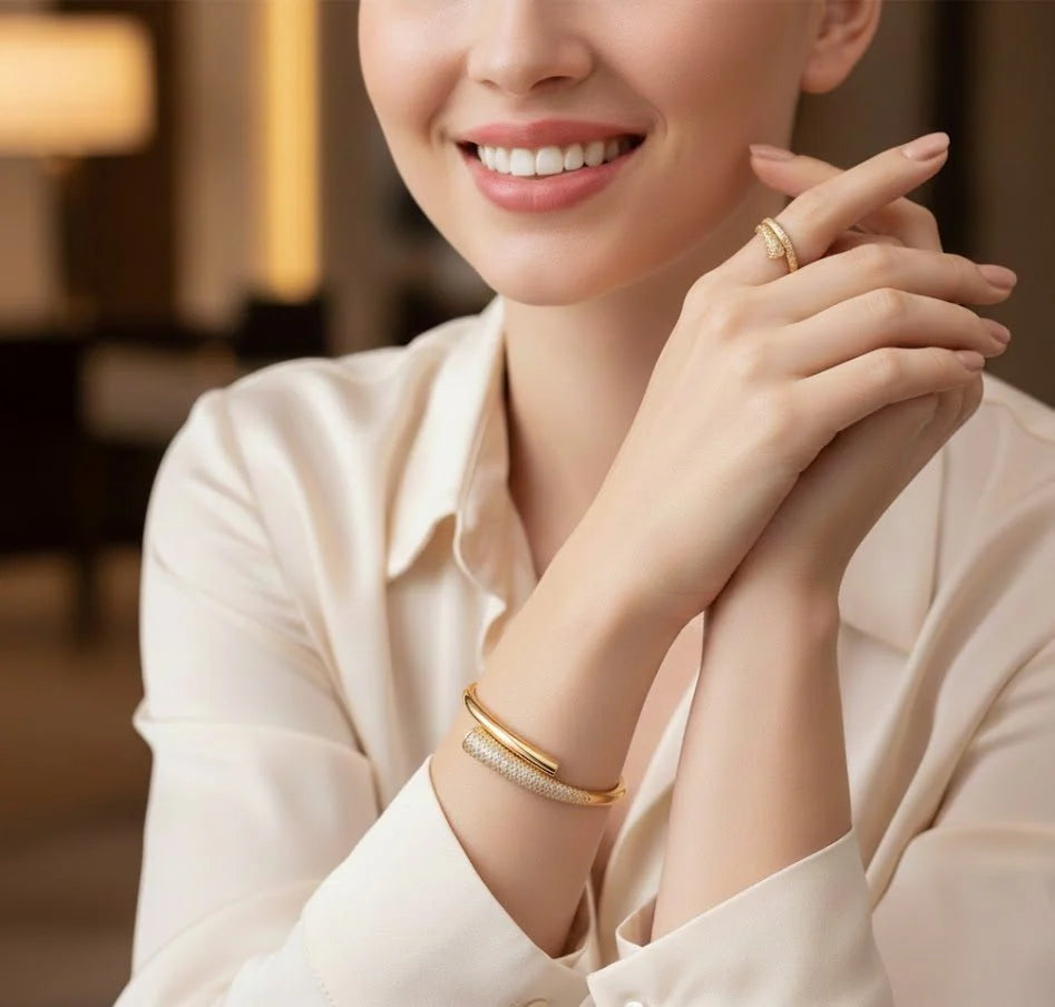 Woman wearing gold jewelry including a ring and bracelet, with a blurred indoor background.